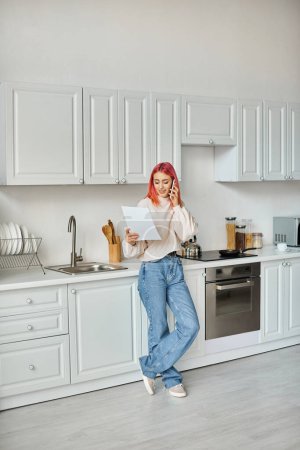 Photo for Cheerful beautiful  woman in comfy attire with pink hair talking by phone and looking at papers - Royalty Free Image