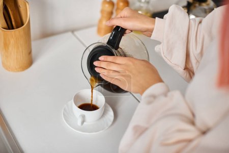 Foto de Vista recortada de la mujer joven en la ropa cotidiana verter café caliente en la taza en casa - Imagen libre de derechos