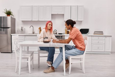 Foto de Atractivo joven pareja multirracial en atuendos casuales hablando entre sí en la cocina en casa - Imagen libre de derechos