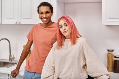 Foto de Bien parecido alegre diversa pareja posando juntos y sonriendo a la cámara en la cocina en casa - Imagen libre de derechos