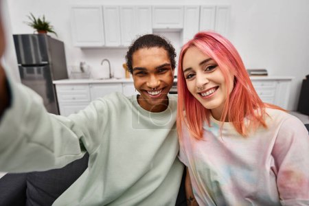 Foto de Alegre atractivo multicultural pareja en casual atuendo tomando selfies y sonriendo a la cámara - Imagen libre de derechos