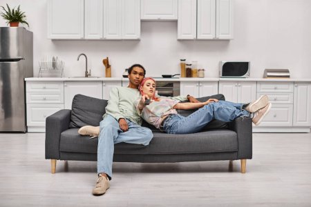 gut aussehendes multikulturelles Paar in Hauskleidung, das Zeit miteinander verbringt und zu Hause Filme anschaut
