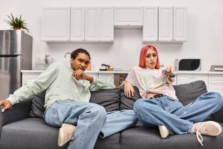 Foto de Aterrorizada pareja multirracial en atuendos casuales viendo películas de terror en casa en la sala de estar - Imagen libre de derechos