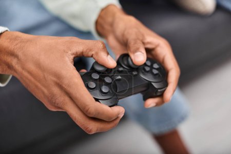 Foto de Vista recortada de gamepad moderno en manos de un joven afroamericano jugando juegos en la sala de estar - Imagen libre de derechos