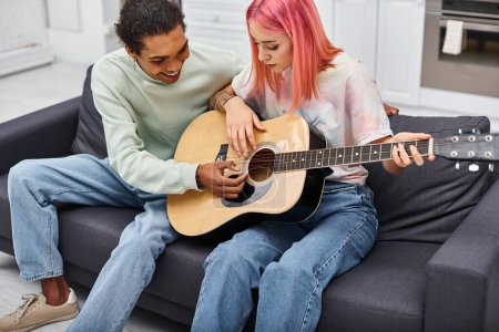 Foto de Guapo jolly africano americano hombre enseñando a su novia a tocar la guitarra mientras que en casa - Imagen libre de derechos