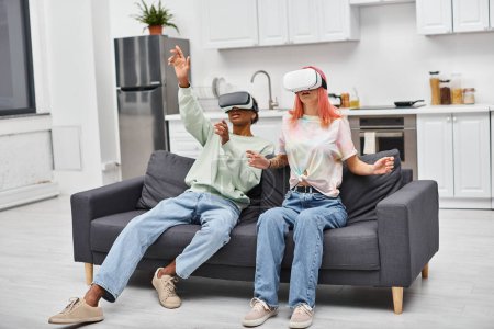 attraktive junge interrassische Paar in bequemen Klamotten sitzt auf dem Sofa zu Hause in ihren VR-Headsets