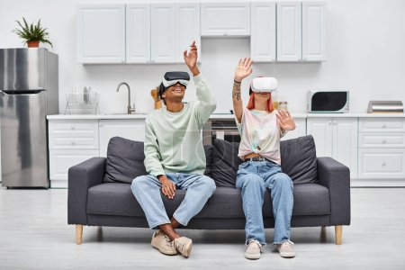 good looking jolly interracial couple sitting on sofa in living room at home with VR headsets