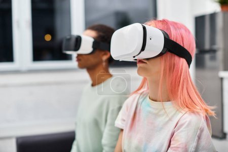 focus on pink haired woman sitting next to her blurred african american boyfriend wearing VR headset