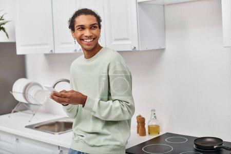 Foto de Guapo hombre afroamericano alegre en suéter casual blanco sosteniendo teléfono inteligente y mirando hacia otro lado - Imagen libre de derechos