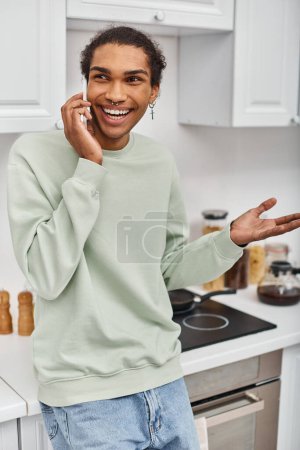 Téléchargez les photos : Attrayant homme afro-américain joyeux en pull vert occasionnel parler par téléphone et détourner les yeux - en image libre de droit