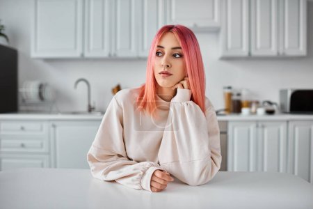 Téléchargez les photos : Belle femme joyeuse avec des cheveux roses en tenue décontractée assis et regardant loin dans la cuisine - en image libre de droit