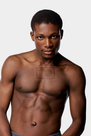 A shirtless African American man poses gracefully in a studio against a white backdrop during his beauty routine.