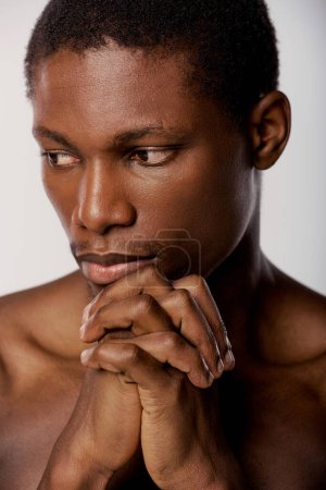 Ein hemdloser afroamerikanischer Mann mit Händen auf der Brust in einem Studio mit weißem Hintergrund, der ruhige Zuversicht ausstrahlt.