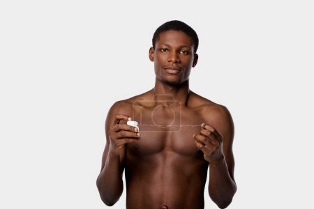 Hombre afroamericano sin camisa sosteniendo hilo dental, promoviendo la rutina de bienestar y belleza.