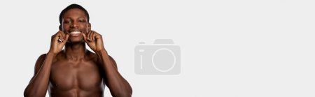 Shirtless African American man in a studio, flossing teeth in a vulnerable gesture. White background.