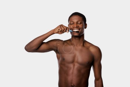 An African American man is energetically brushing his teeth in a studio against a white background.