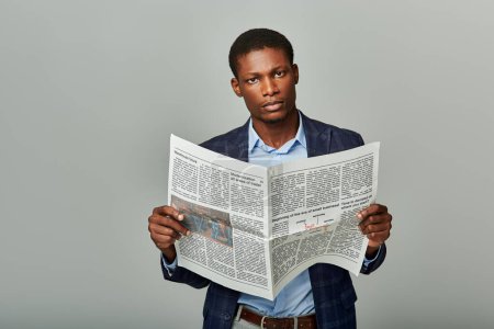 African American man in checkered blazer reading a newspaper on a grey background.