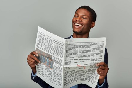 Ein gutaussehender afroamerikanischer Mann im karierten Blazer liest eine Zeitung und lacht herzlich.