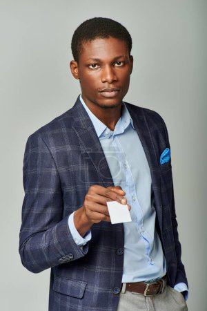 Hombre de negocios afroamericano con un elegante traje que presenta una tarjeta de visita sobre un fondo gris.