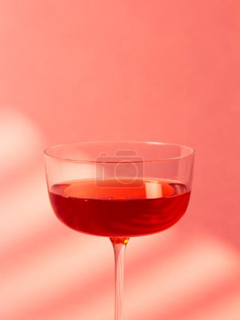Una imagen elegante y elegante de una copa de cóctel llena de líquido rojo sobre un fondo rosa vibrante. Esta composición moderna es perfecta para temas de elegancia, estilo y bebidas sofisticadas..