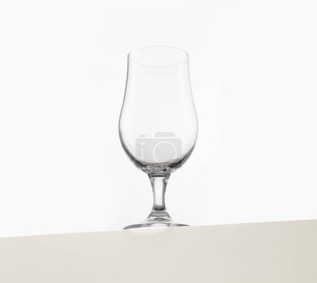 Una copa de vino clara y vacía se muestra elegantemente sobre un fondo blanco liso. El diseño elegante y sencillo de la cristalería enfatiza sus líneas limpias y transparencia