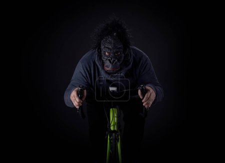 Eine Person mit Gorillamaske fährt auf einem Fahrrad vor dunklem Hintergrund. Die ungewöhnliche Kombination aus Maske und Aktivität schafft eine humorvolle und surreale Szene, perfekt für Themen der Komik, Neuheit und Kreativität..