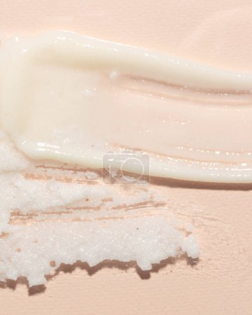 Nahaufnahme einer Hautpflegeprodukttextur mit einer glatten, cremigen Feuchtigkeitscreme neben einem körnigen Peeling auf sanftem rosa Hintergrund. Perfekt zur Darstellung von Beauty-Routinen und kosmetischen Details in hochwertigen, detaillierten Bildern.