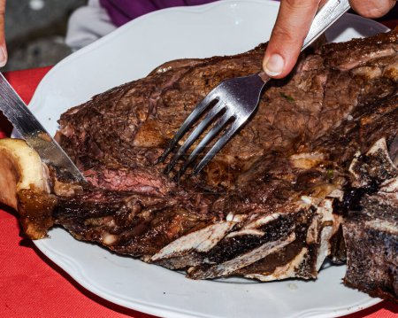 Téléchargez les photos : Maîtrise culinaire : les mains de la femme tranchent dans un délicieux steak de côtes de barbecue avec précision - en image libre de droit