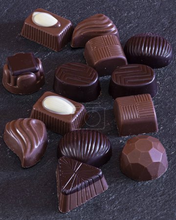 An assortment of gourmet chocolates in various shapes and sizes, featuring rich dark and creamy white chocolate, elegantly displayed on a dark slate background