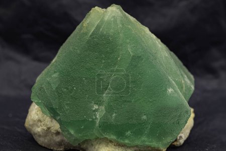 Robuster und strahlend grüner Fluoritkristall, der auf einem kontrastierenden dunklen Hintergrund zur Geltung kommt und seine scharfe geometrische Form und seine tiefe, fesselnde grüne Farbe hervorhebt