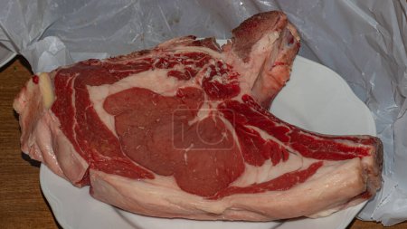 A premium cut of raw beef steak, rich in marbling and color, presented on a white plate, ready for culinary preparation