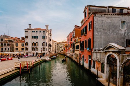 Wenecja, Włochy - październik 2022: wenecka gondola płynąca charakterystycznym kanałem z kolorowymi budynkami o zachodzie słońca
