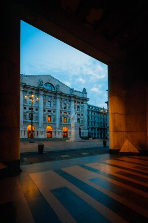 Téléchargez les photos : Milan, Italie - Septembre 2023 : Piazza Affari à Milan avec statue en marbre de Maurizio Cattelan à travers le portique du bâtiment en face de la Bourse italienne à l'aube - en image libre de droit