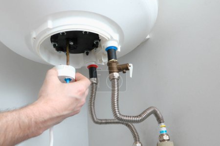 La main d'un plombier installe un thermostat dans une chaudière après réparation. Réparation de chauffe-eau.