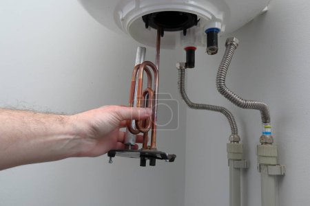 Photo for Man's hand putting a new water heater in a boiler. - Royalty Free Image