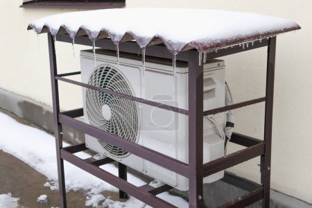 Téléchargez les photos : Thermopompe montée sur le mur d'une maison et recouverte de neige par une journée froide d'hiver. - en image libre de droit