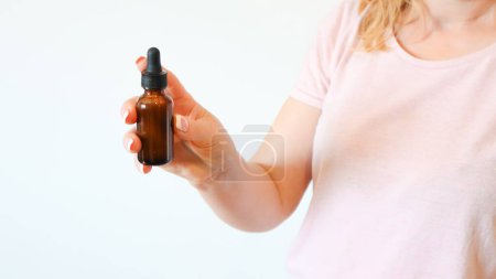 Téléchargez les photos : Women's hands hold bottle of amber glass with cosmetic face serum on white background. Young woman holding brown glass bottle with dropper with spa cosmetics. - en image libre de droit