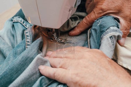 Photo for Elderly male tailor sews on a sewing machine. Tailor sewing cloth with sewing machine at sewing workshop - Royalty Free Image