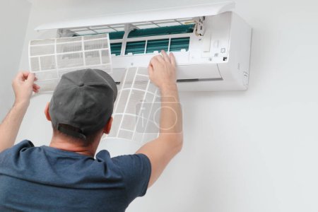Air conditioner service indoors. Male Technician removing air filter of the air conditioner for cleaning. Air conditioner service and maintenance