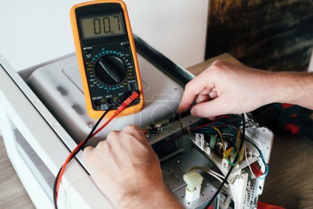 Photo for A repair engineer uses a multimeter to check the circuits of a microwave oven, looking for a fault. Diagnostics repair of microwave oven. - Royalty Free Image