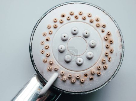 Silver round shower head with hard water deposits, limescales closeup. Calcified shower due to hard water. Selective focus on hard water deposit.