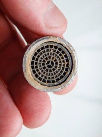 Hand is holding a chrome faucet aerator covered with lime scale. Faucet contaminated with calcium. Limescale on tap mixer. Polluted and calcified water in our homes.