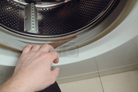 Schmutzige, verschimmelte Waschmaschine versiegelt Gummi. Die Person überprüft den Schmutz auf dem Gummi einer Waschmaschine. Geschnittene Hand haltende Waschmaschine. Gummidichtung auf Waschmaschinentrommel