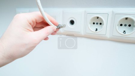 A man inserts a coaxial cable plug into a TV antenna socket. Inserts the antenna cable to the TV outlet. Close-up, selective focus.