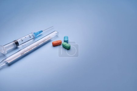 Eine medizinische Plastikspritze und ein Quecksilberthermometer aus Glas werden auf blauem Untergrund fotografiert, eine diagonale Ansicht von oben, der Begriff Medizin und Gesundheit