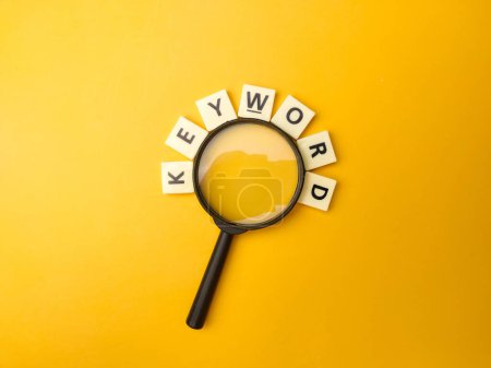 Foto de Magnifying glass and toys word with the word KEYWORD on yellow background - Imagen libre de derechos