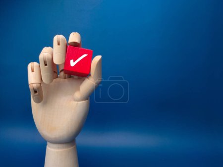 Photo for Wooden hand holding red cube with correct sign on blue background. Business concept. - Royalty Free Image