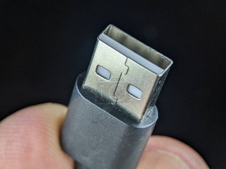 Téléchargez les photos : Closeup finger holding USB charger cable on a black background. - en image libre de droit