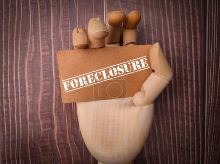 Photo for Wooden hand holding card board with the word FORECLOSURE on a wooden background. - Royalty Free Image