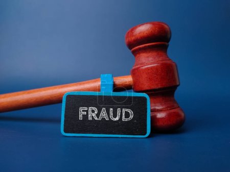 Photo for Gavel and wooden board with the word FRAUD on a blue background. - Royalty Free Image